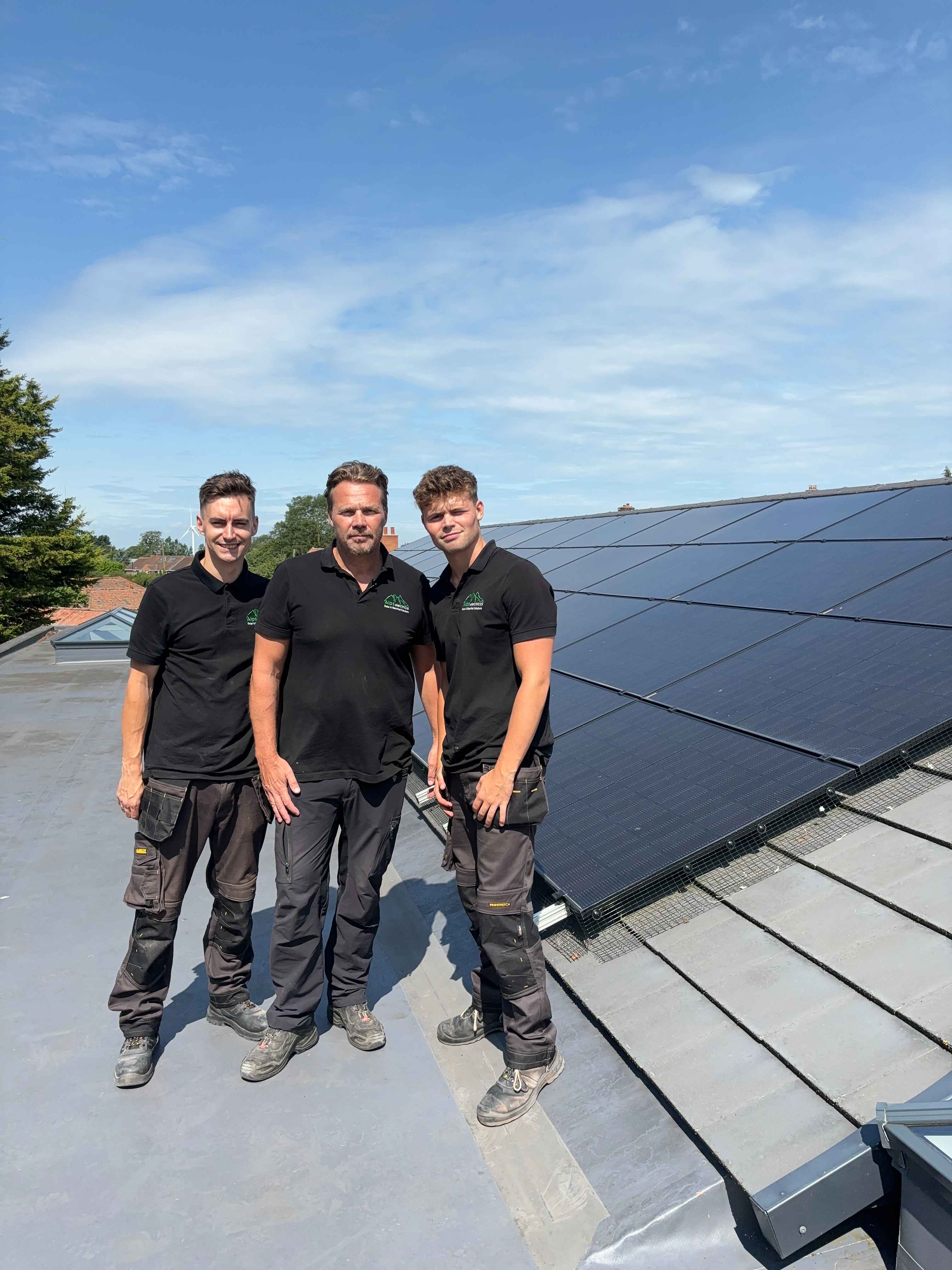 ALPS team members on a rooftop with solar panels against blue sky